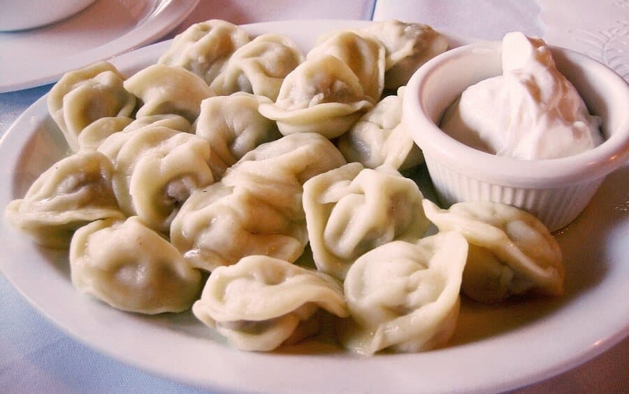 A plate of boiled pelmeni with a dish of sour cream